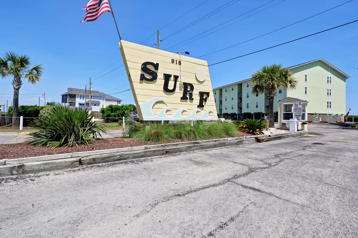 A cheerful exterior scene with a large 'SURF' sign, palm trees, a vibrant green building, and a road inviting exploration. The relaxed setting hints at the lively Surf City neighborhood, with easy access to local attractions and beach activities.