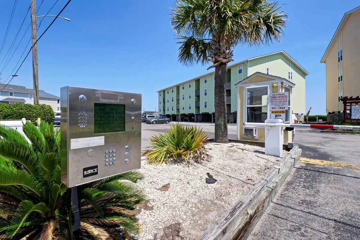 The condo's entrance is framed by palm trees and a well-maintained facade, with an inviting walkway and landscaped area. The entry intercom hints at both privacy and secure access for groups arriving together.