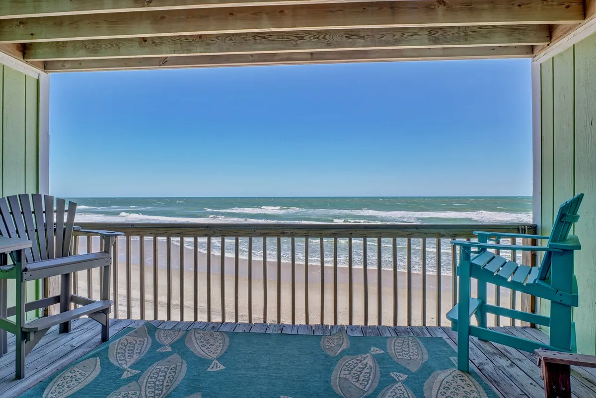 A tranquil private deck featuring two chairs and a decorative rug, positioned to enjoy unobstructed ocean views beyond a wooden railing. The setting is perfect for sipping coffee, reading, or relaxing while watching the sun rise or set over the Atlantic.
