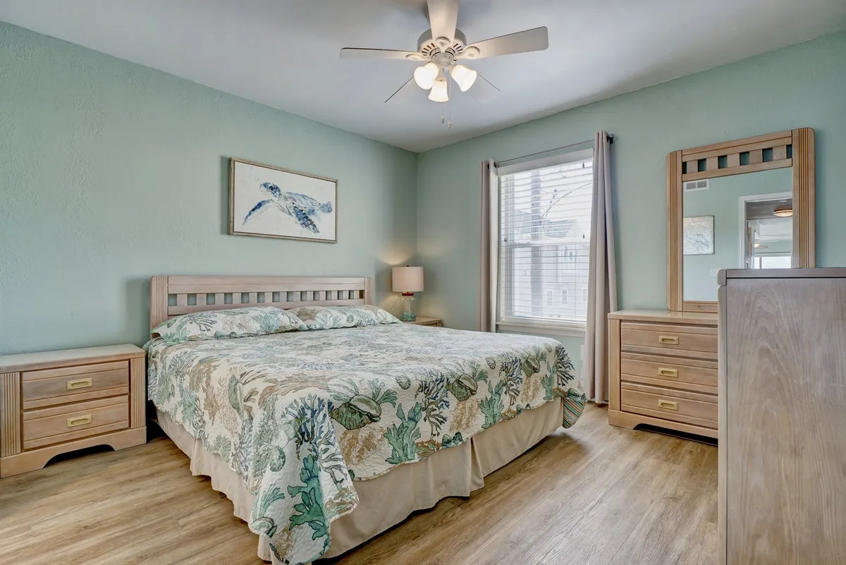 A tranquil master bedroom featuring a bed with floral bedding, light wood furniture, and a window that allows in abundant natural light. The serene decor and calming colors create a relaxing atmosphere ideal for restful sleep.