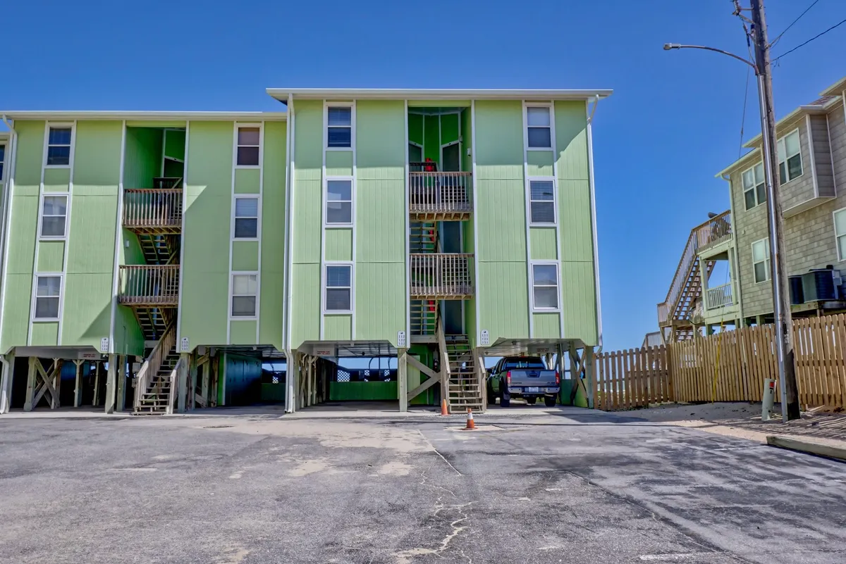 A vibrant exterior shot of a colorful green building featuring staircases and open space beneath, set in an inviting, family-friendly environment. The scene suggests opportunities for gatherings, outdoor games, and casual relaxation close to the beach.