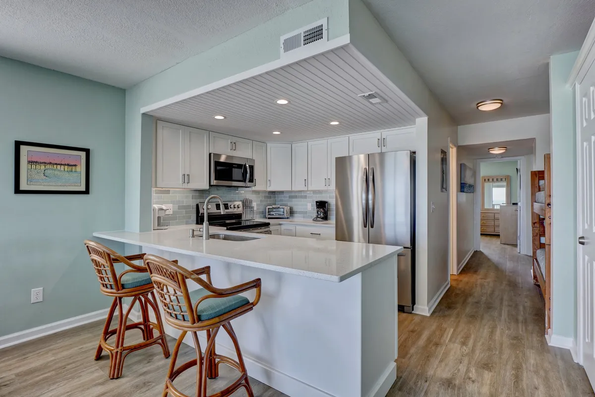 A close-up of the kitchen island with comfortable bar stools, sleek stainless steel appliances, and an open sightline to the rest of the living space. The setting is bright and functional, with plenty of room for preparing meals or enjoying a casual breakfast at the counter.