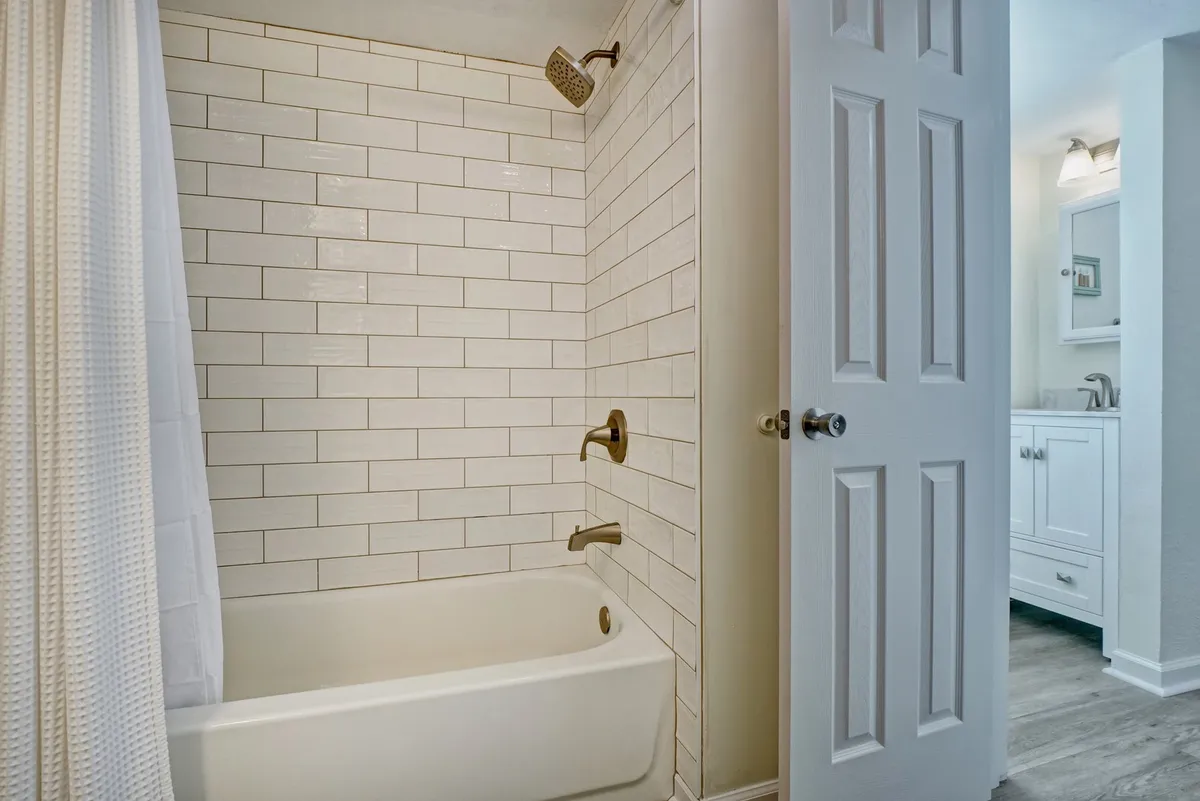 A bright, inviting bathroom featuring a bathtub with showerhead, tiled walls, and a modern vanity. The space feels serene and well-equipped for both quick morning routines and relaxing evening baths.
