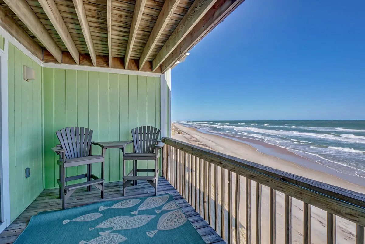 A serene view from the private wooden deck, furnished with comfortable deck chairs and a decorative rug, overlooking the sparkling ocean. The scene invites relaxation and offers a front-row seat to sunrises, dolphin watching, or stargazing at night.
